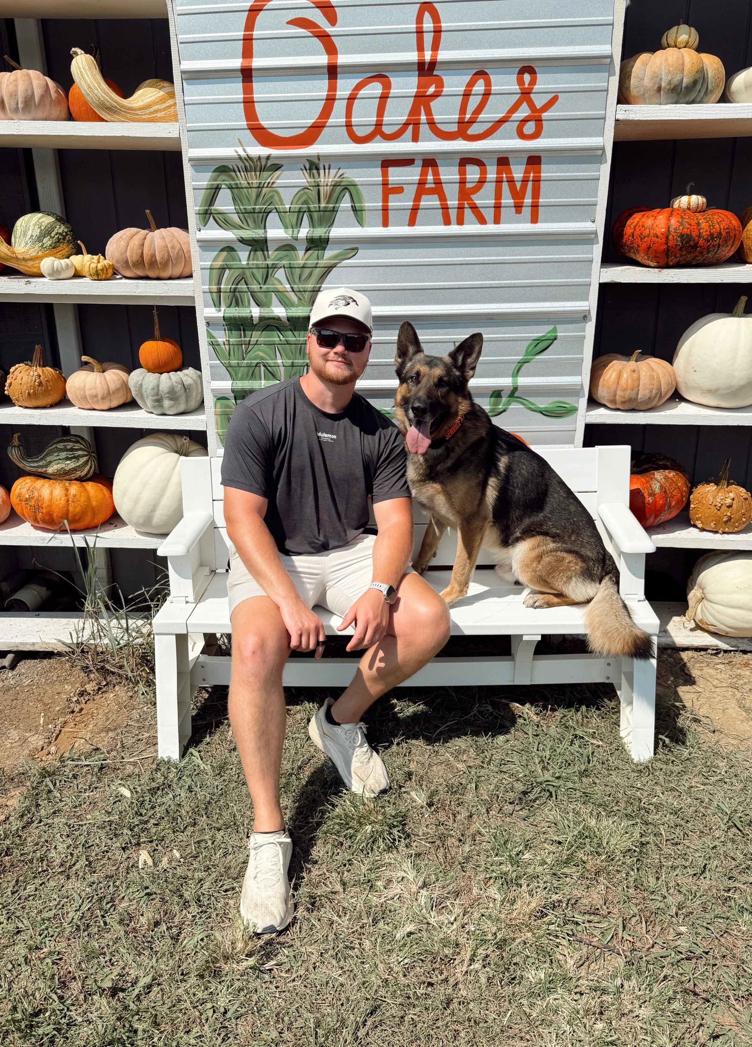 Clayton with his dog on a bench in front of a Cares Farm sign surrounded by pumpkins